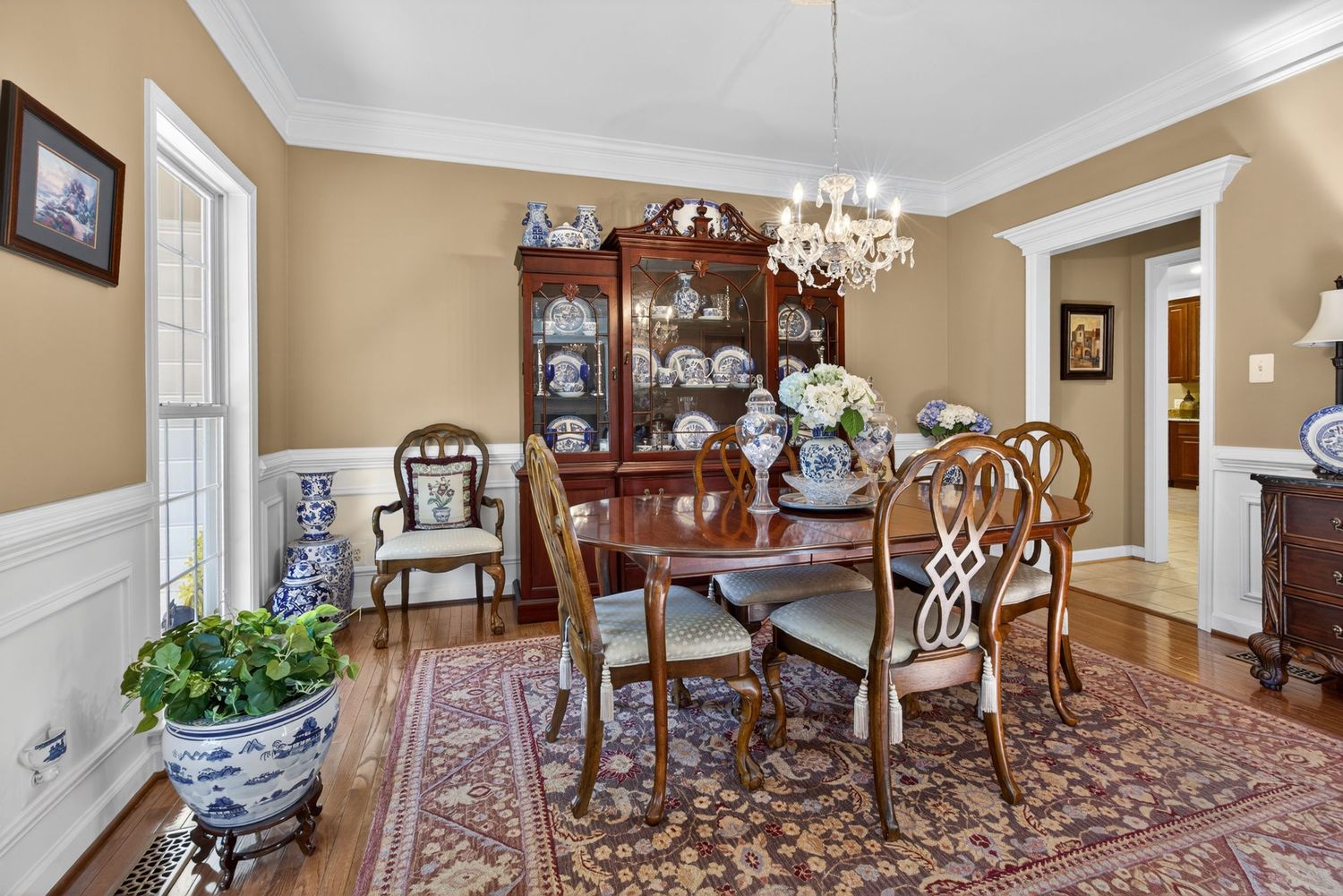 Elegant dining room with chandelier, mahogany table, ornate chairs, china cabinet, and Persian rug on hardwood floors.