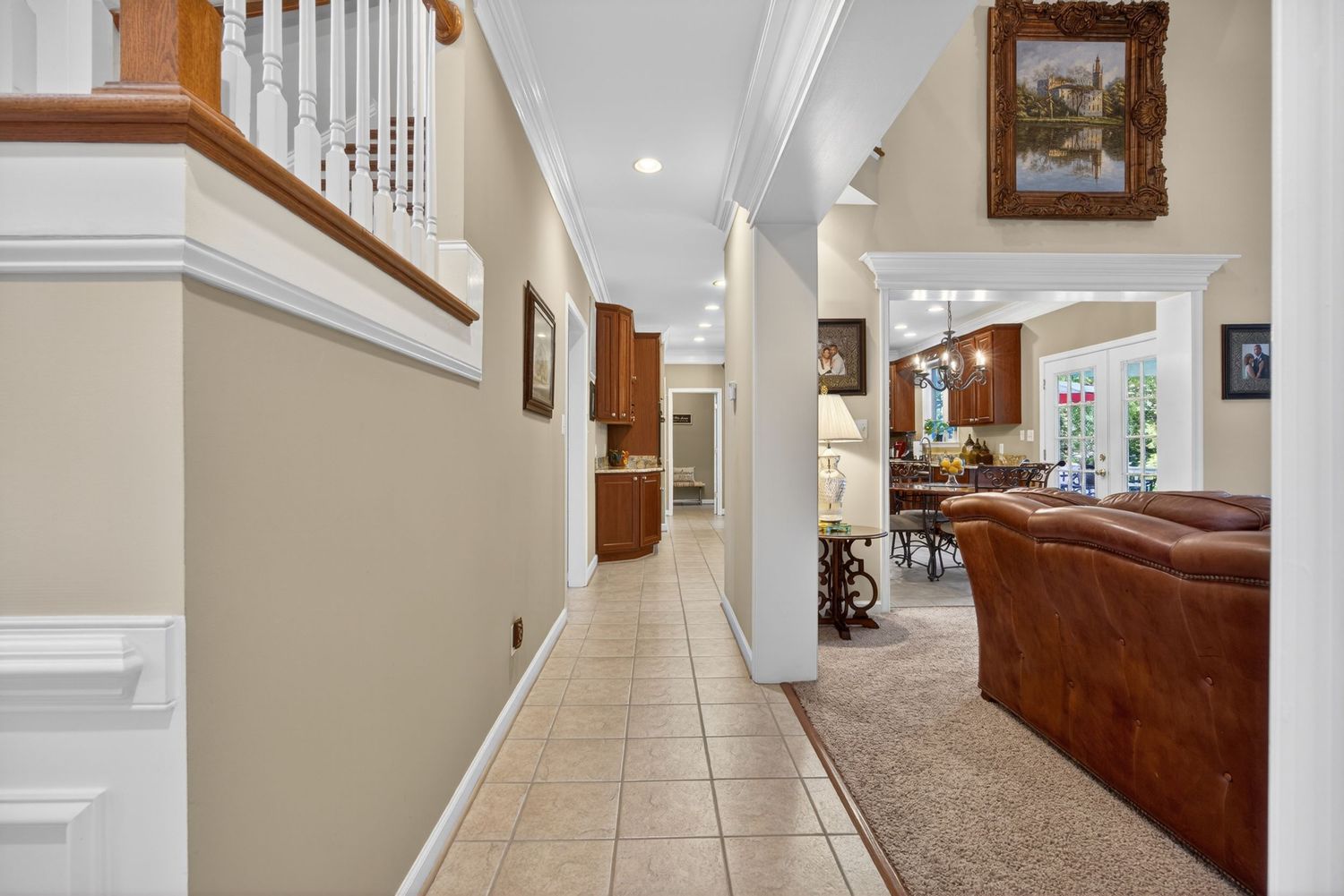 Elegant hallway with beige walls, tile floors, decorative columns, and an open view to a cozy living room with leather sofa.