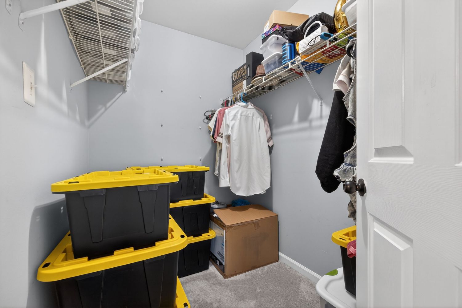 Walk-in closet with gray walls, yellow storage bins, shelving, and hanging clothes rod in a residential home.