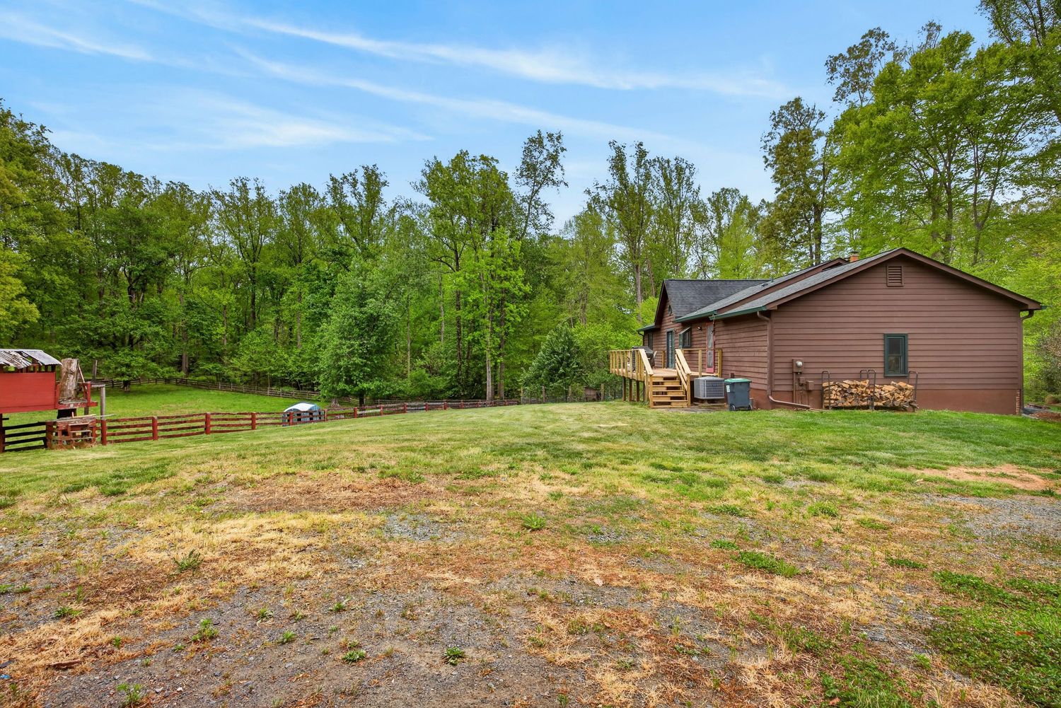 Brick home with large green lawn surrounded by lush forest trees and wooden fence in a rural setting.