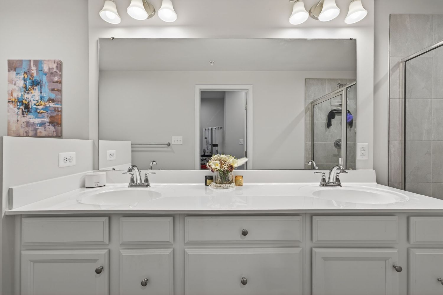 Modern bathroom with double vanity, white cabinets, large mirror, and quartz countertop with dual sinks.