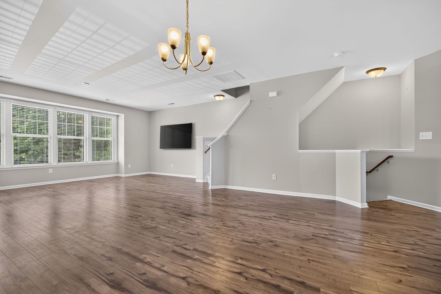Spacious open-concept living room with hardwood floors, chandelier, and staircase in a modern home.