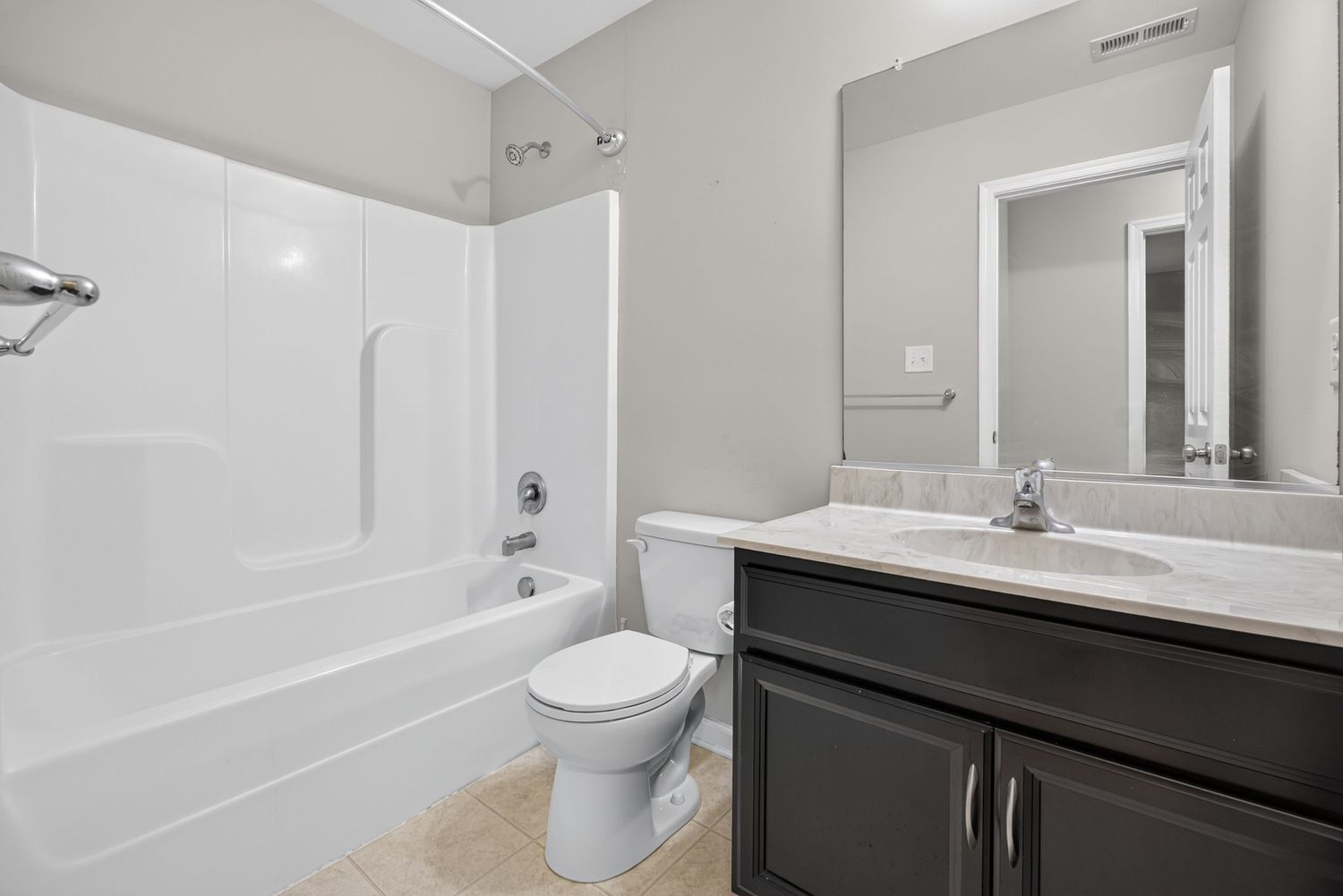 Modern bathroom with white bathtub, toilet, dark vanity cabinet, and large mirror in a neutral gray interior.
