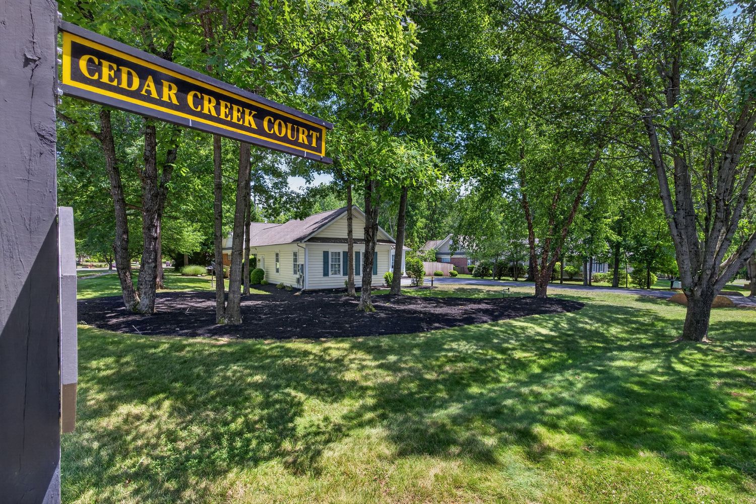 Cedar Creek Court apartment community entrance sign surrounded by lush green trees and well-maintained lawn.