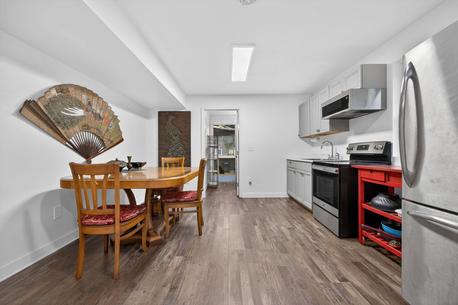 Cozy kitchen and dining area with hardwood floors, stainless steel appliances, round wooden table, and decorative fan wall art.