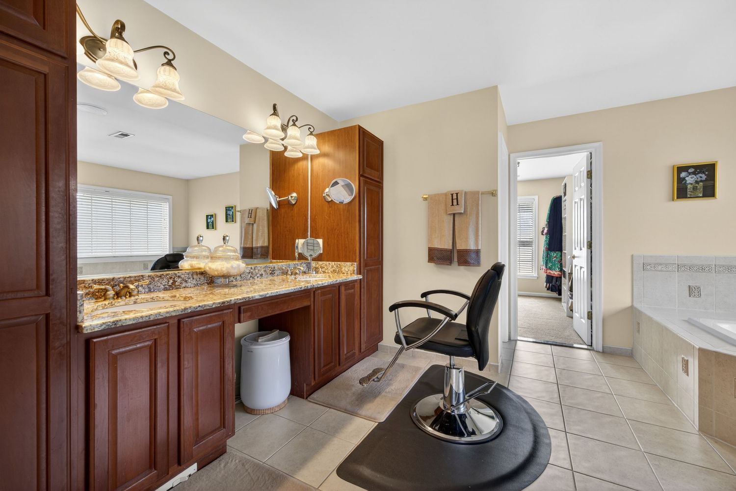 A home hair salon with cherry wood vanity, granite countertop, barber chair, and tile flooring in a bright room.