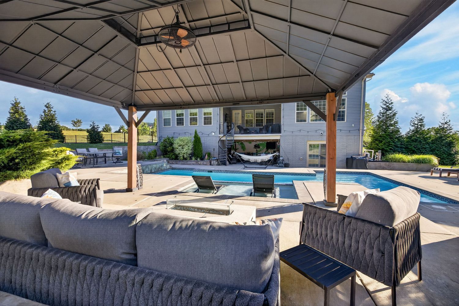 Outdoor covered patio with gray sectional sofa overlooking a sparkling pool and elegant home backdrop.