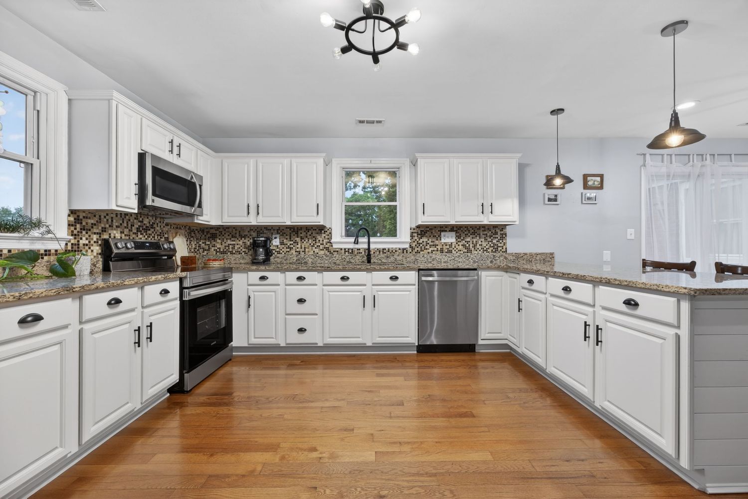 Bright kitchen with white cabinets, granite countertops, stainless steel appliances, mosaic backsplash, and hardwood floors.
