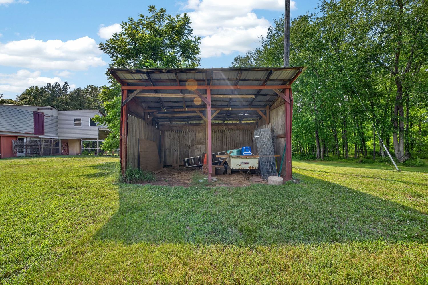 Open metal carport shelter with a truck parked inside, surrounded by lush green grass and trees on a sunny day.