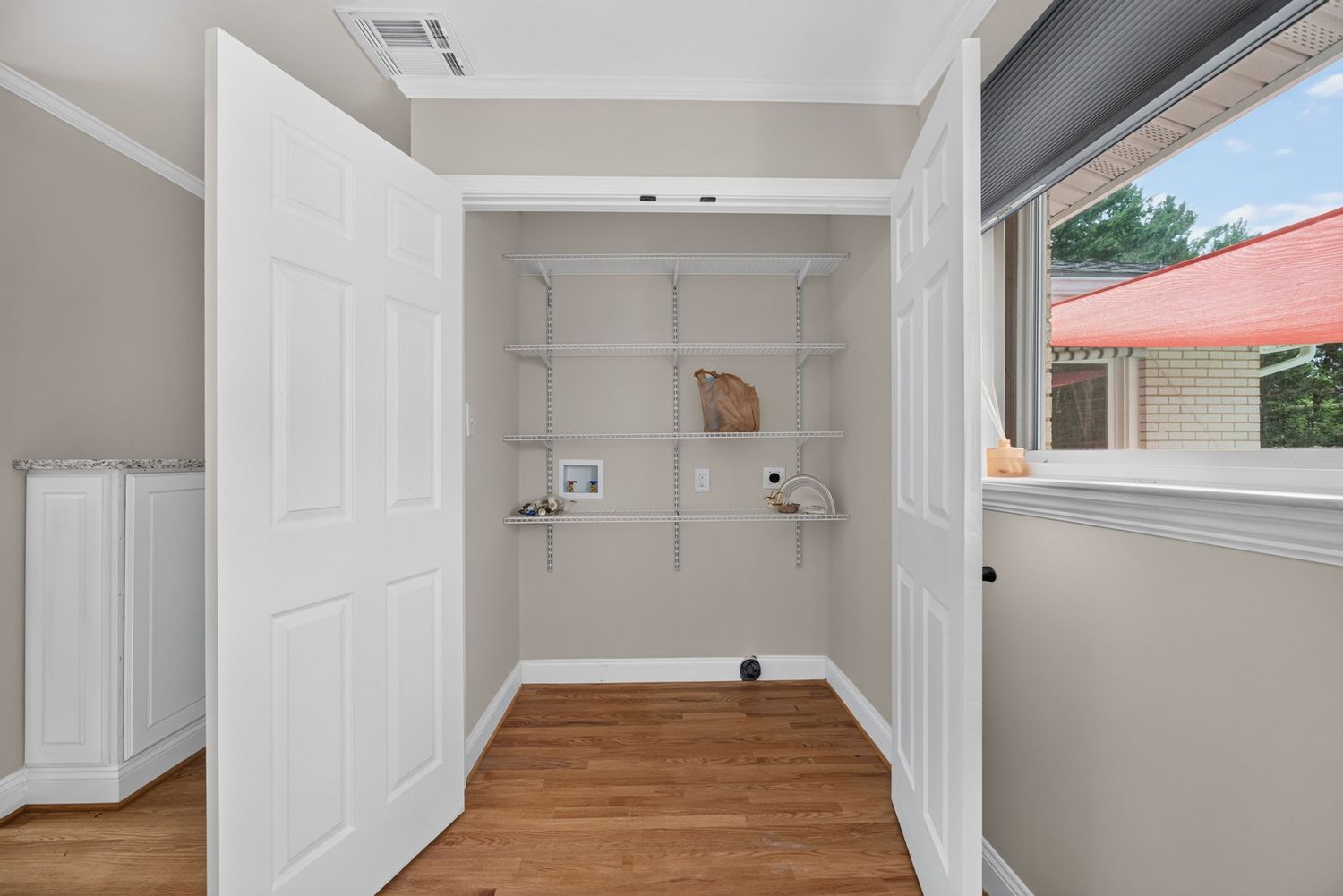 Open walk-in closet with white built-in shelves, hardwood floors, and natural light from a nearby window.