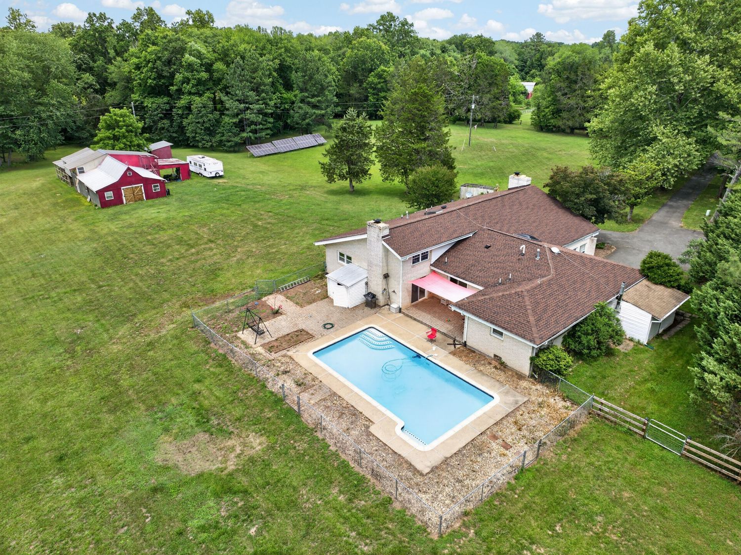Aerial view of a large country home with an in-ground pool, expansive green lawn, and red barn surrounded by mature trees.