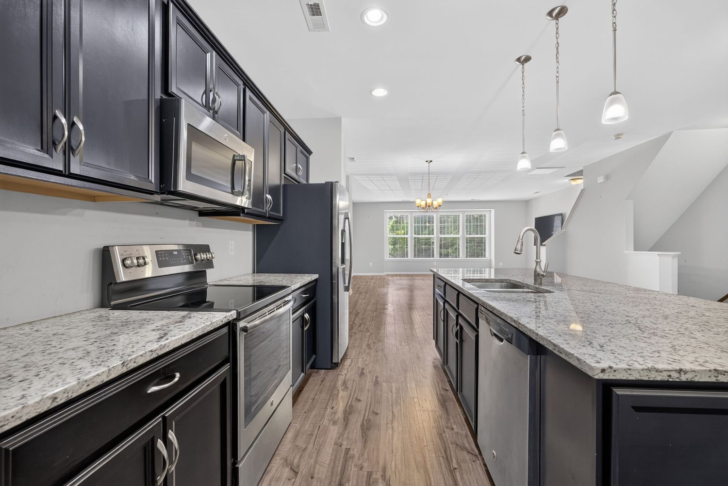 Modern kitchen with dark navy cabinets, granite countertops, stainless steel appliances, and hardwood floors leading to dining area.
