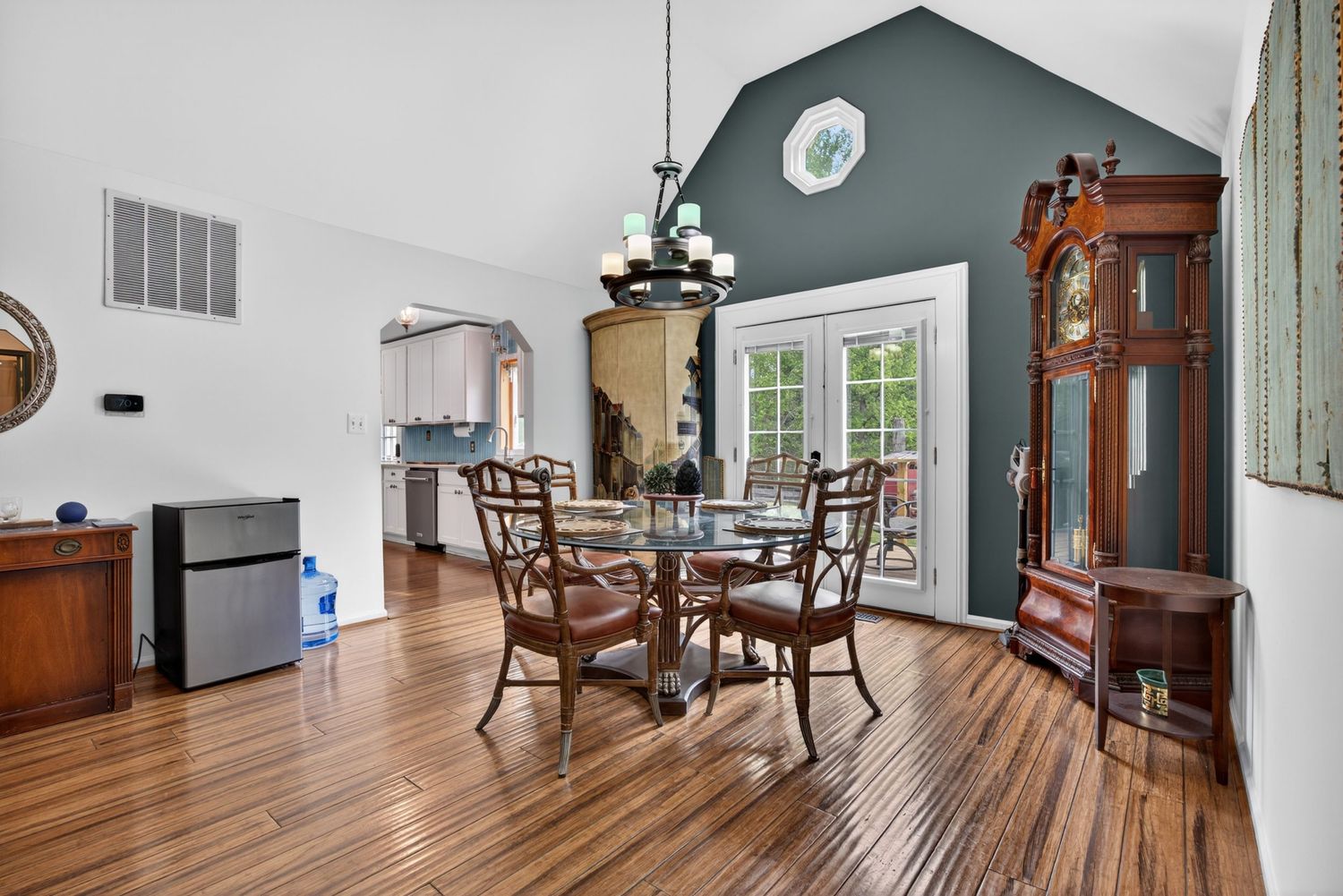 Dining room with hardwood floors, glass table, wooden chairs, grandfather clock, and teal accent wall with vaulted ceiling.