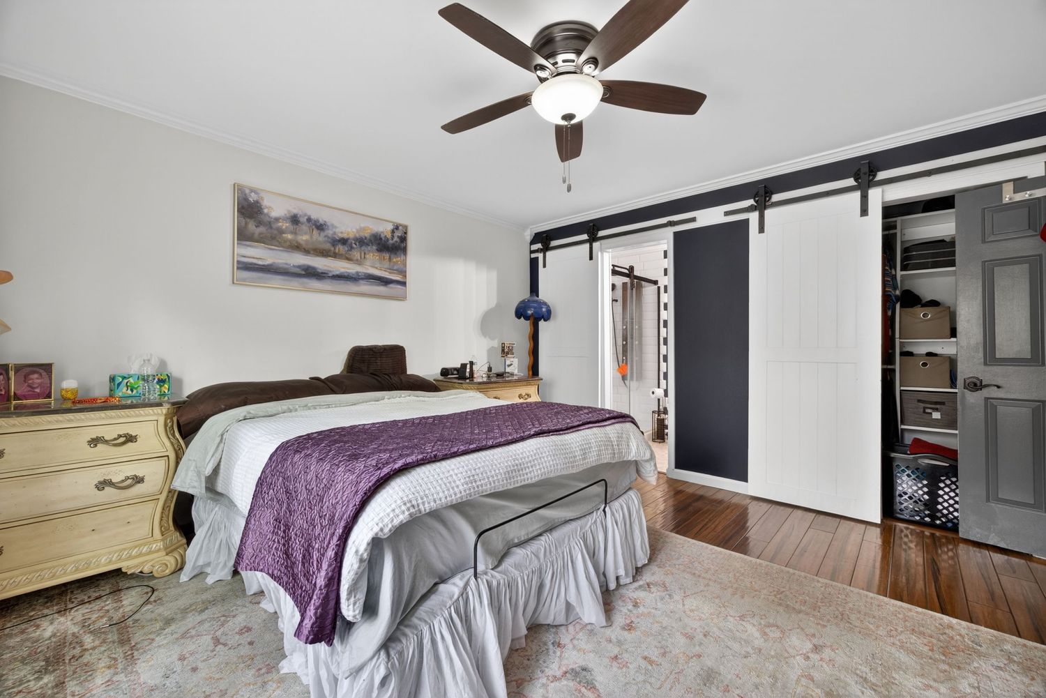 Bedroom with ceiling fan, hardwood floors, barn doors leading to closet, and a large bed with purple accents.
