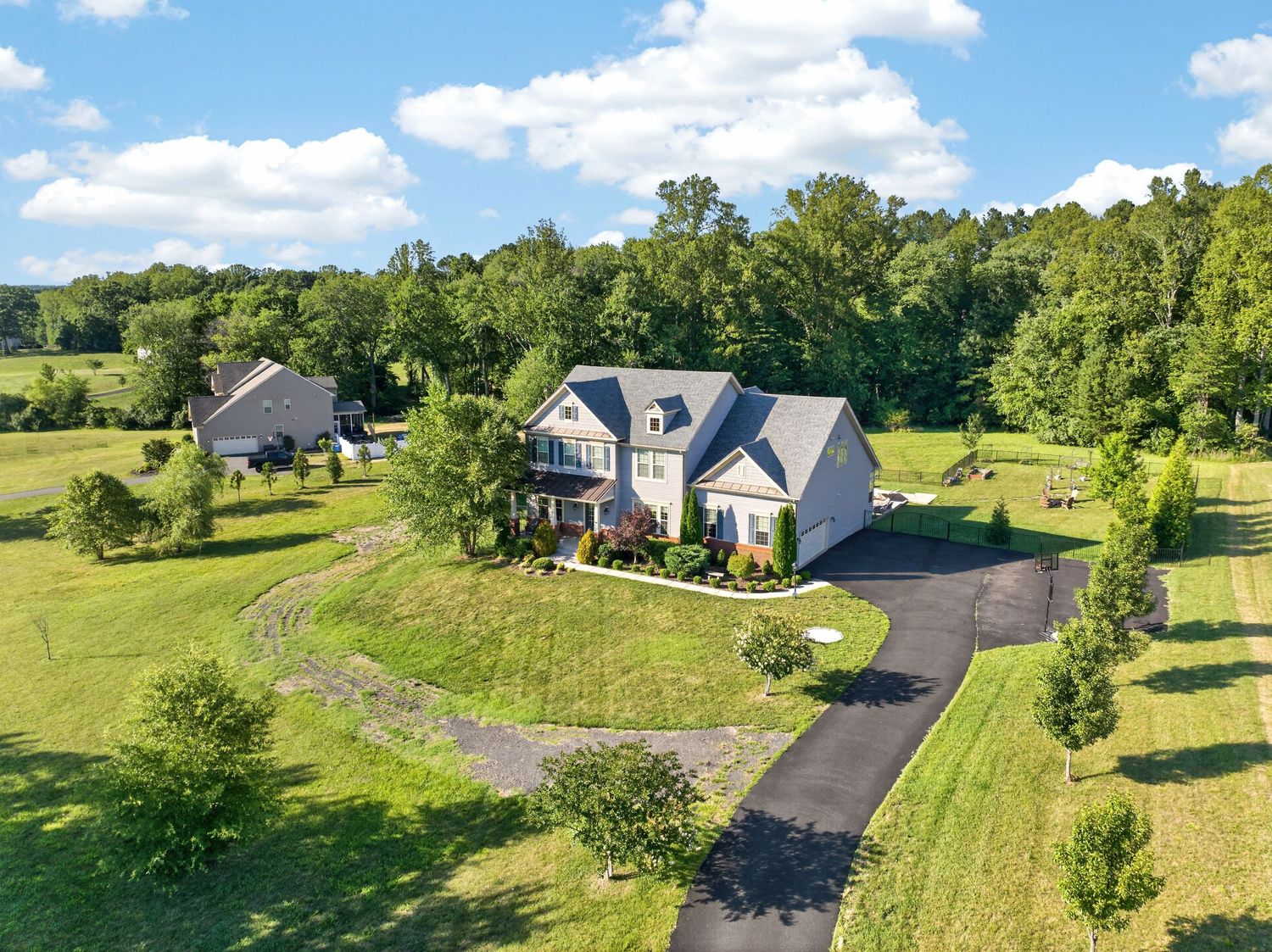 Aerial view of a large two-story home with circular driveway surrounded by lush green trees and open countryside.