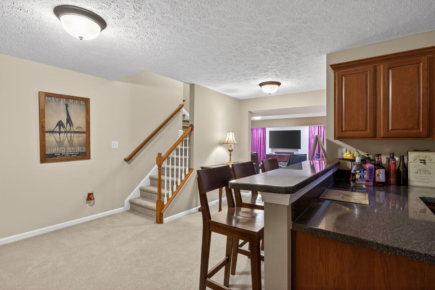 Open-concept kitchen with dark granite counters, cherry cabinets, bar seating, and carpeted living area with staircase.