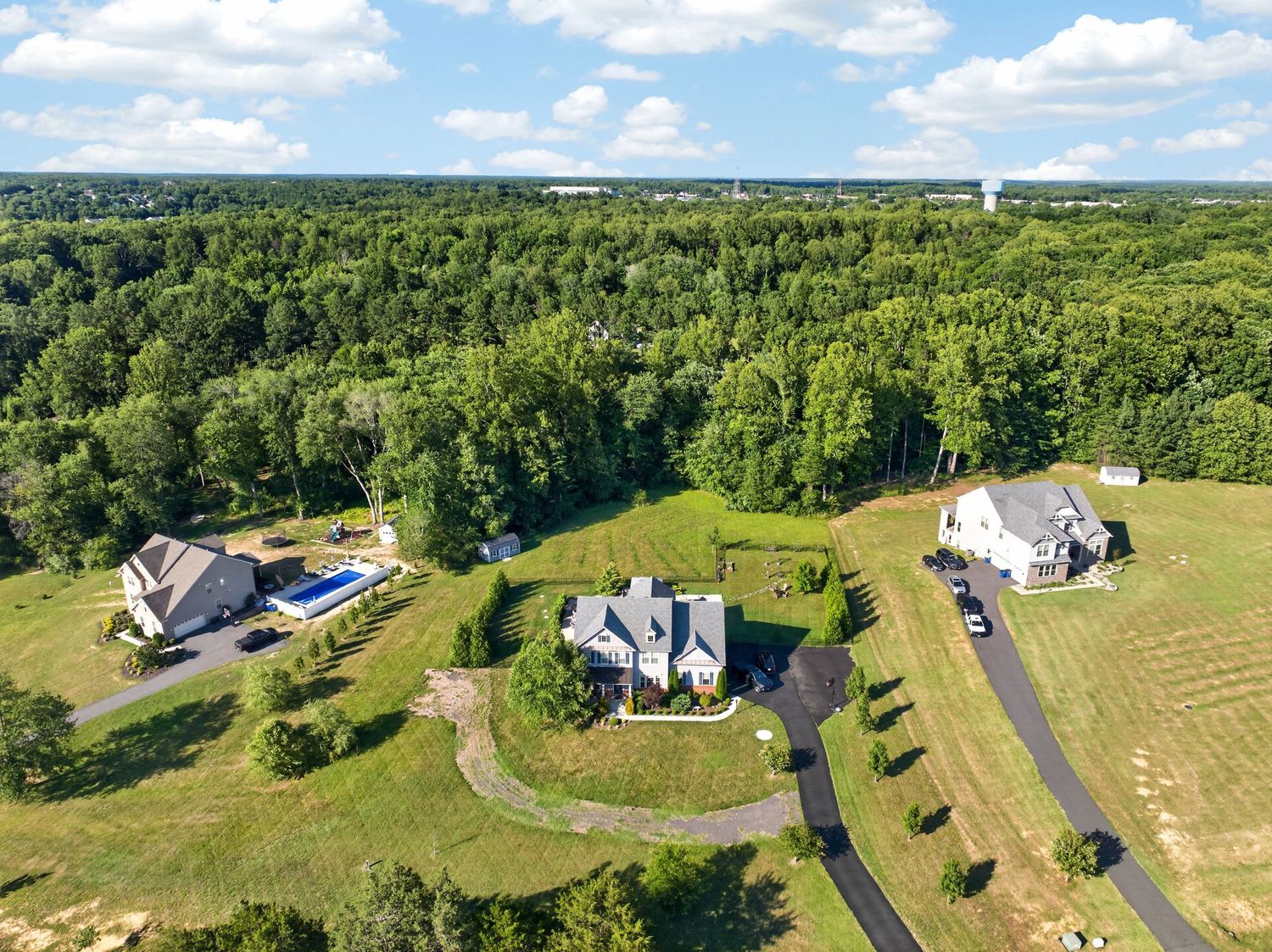 Aerial view of luxury homes surrounded by lush green forest and manicured lawns in a serene suburban estate setting.