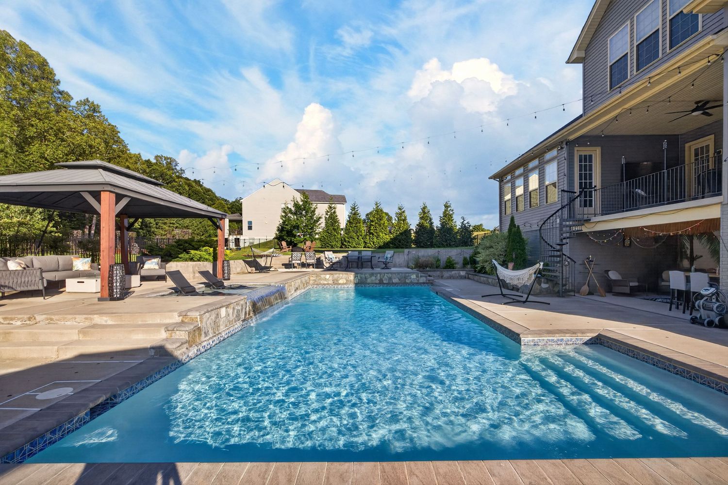 Luxury backyard pool with pergola, stone patio, and elegant home exterior on a sunny day.