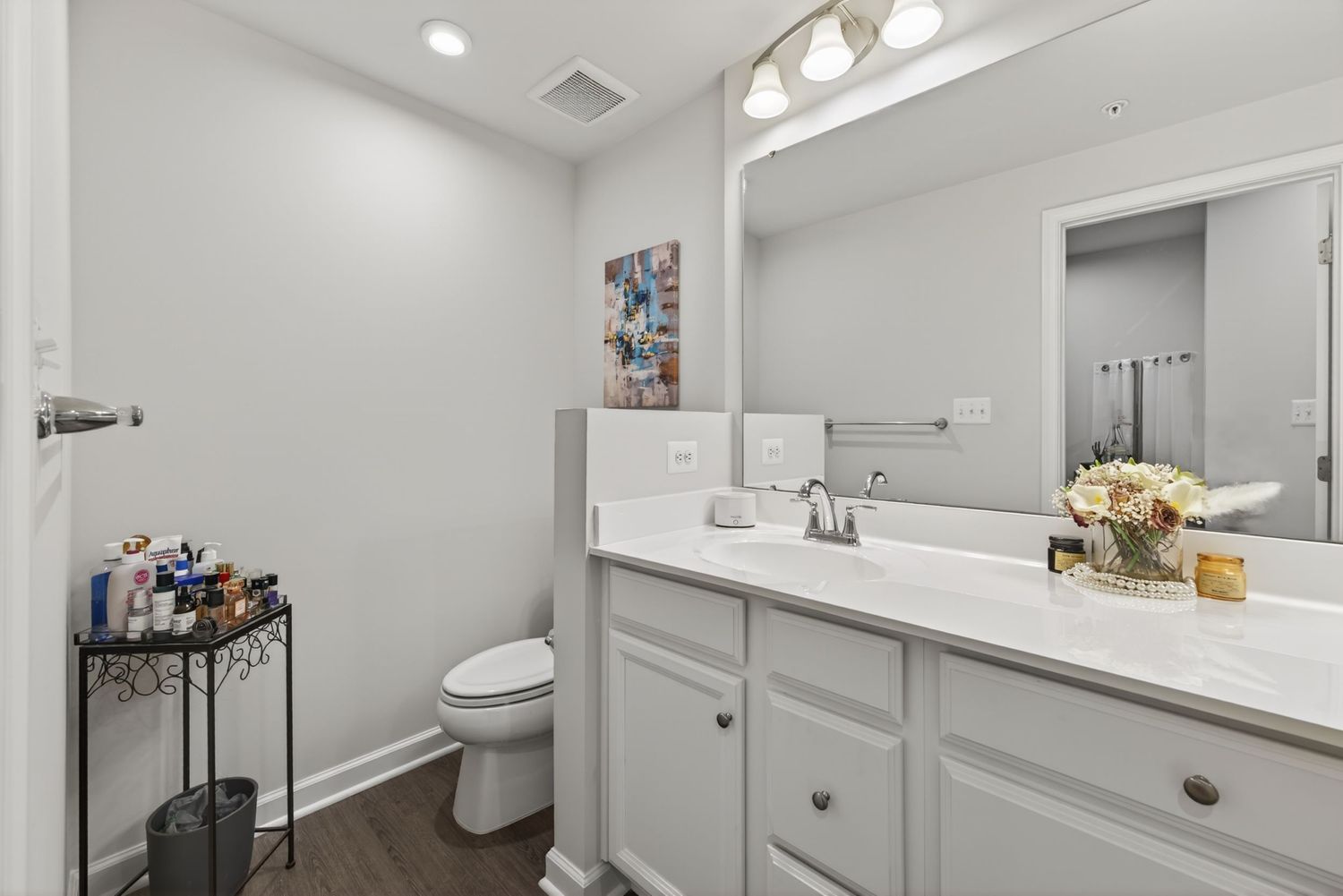 Modern bathroom with white vanity, large mirror, toilet, and dark hardwood floors in a bright, clean space.
