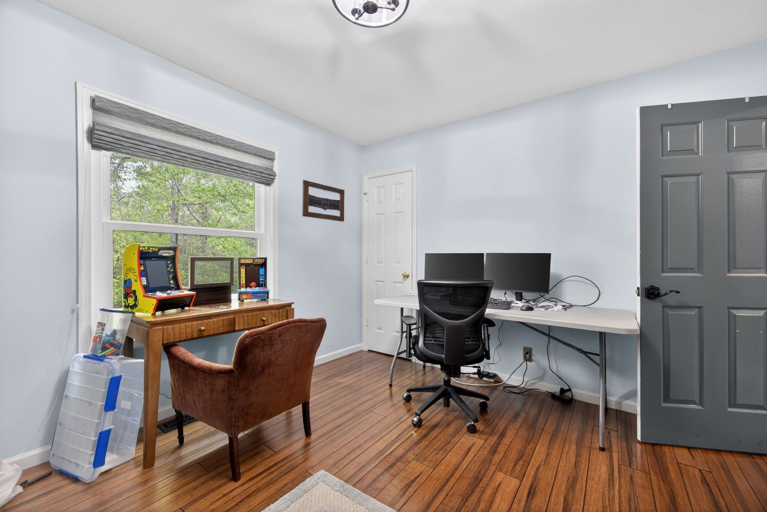 Home office with hardwood floors, two desks, office chairs, and a bright window with natural light.