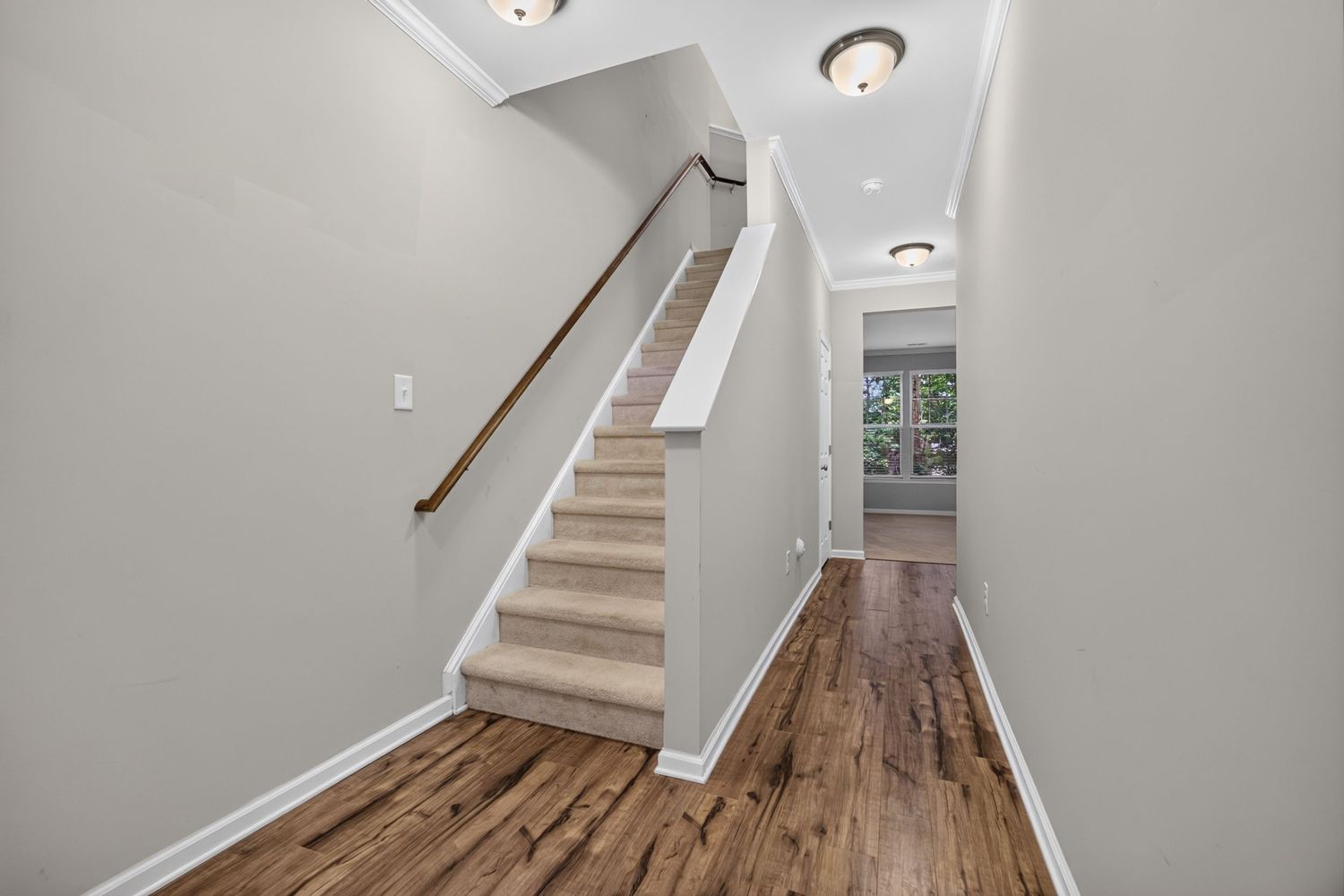 Bright entryway hallway with hardwood floors, white staircase with wood railing, recessed lighting, and a window at the end.