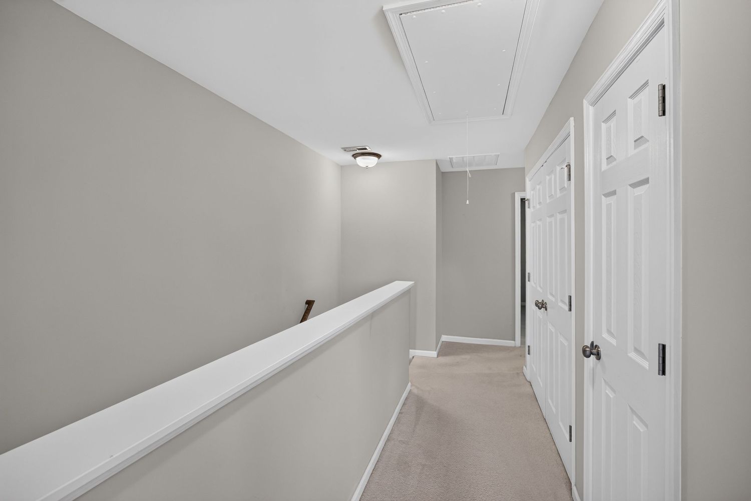 Bright hallway with neutral carpet, white doors, and attic access panel in a modern home.