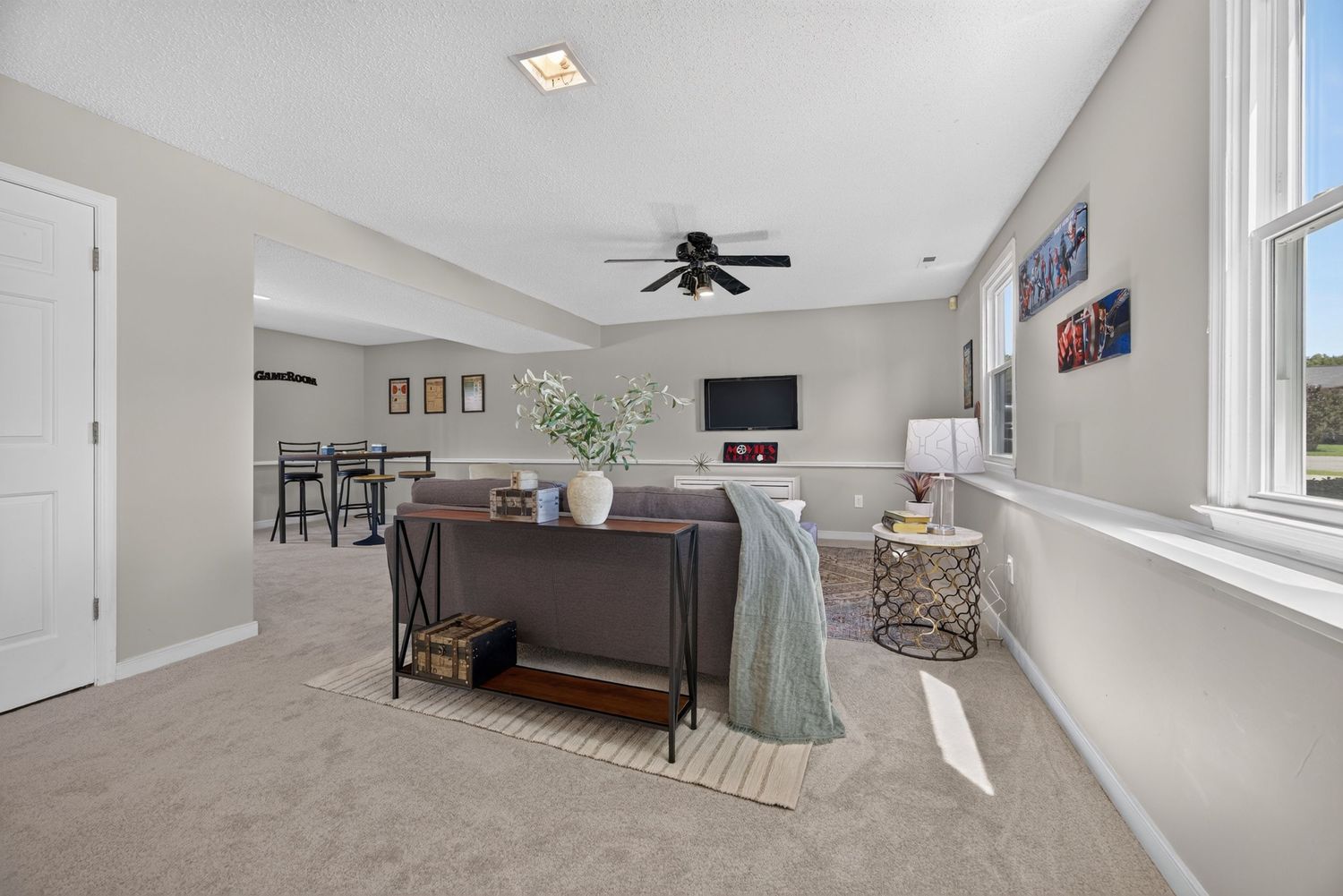 Spacious carpeted living room with ceiling fan, neutral gray walls, dark wood console table, and open layout connecting to dining area.