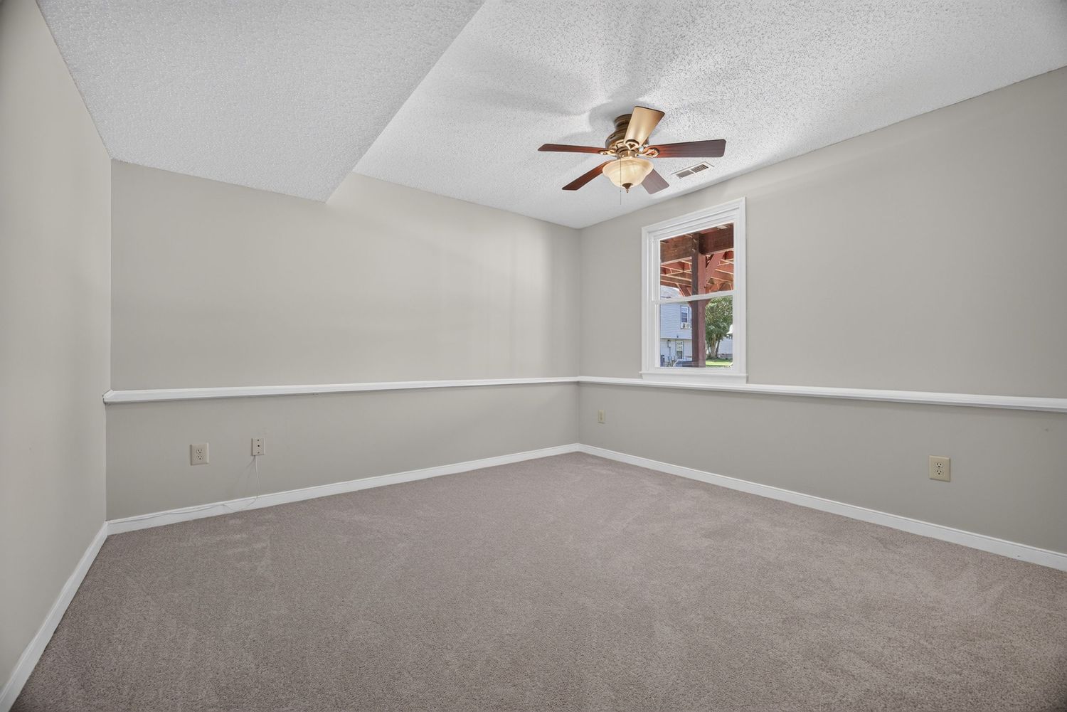 Empty bedroom with light gray walls, ceiling fan, and carpeted floor with natural light from a window.