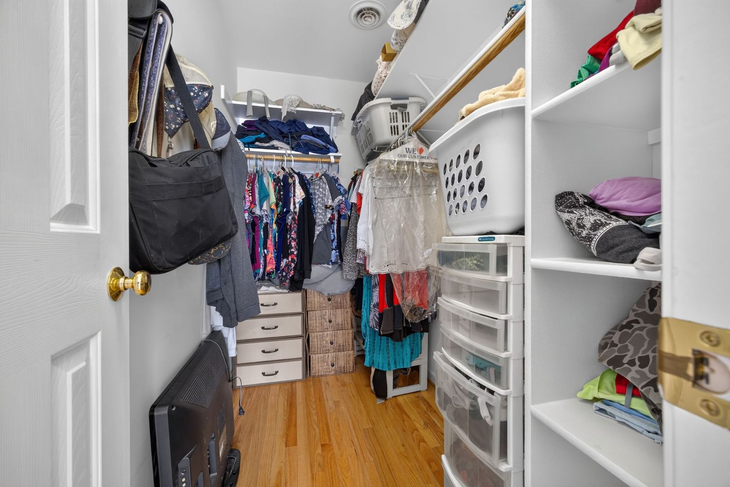 Walk-in closet with hardwood floors, white shelving units, hanging clothes rods, and organized storage space.