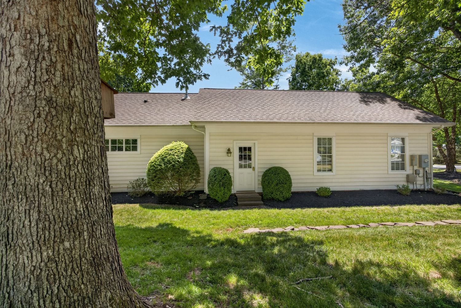 A charming yellow ranch-style home with manicured shrubs, lush green lawn, and mature trees on a sunny day.