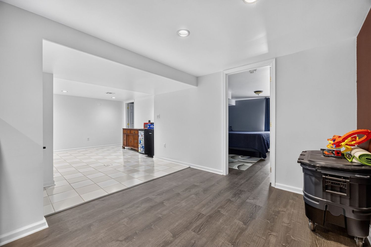 Spacious basement with dark hardwood floors, white walls, recessed lighting, and an open layout leading to additional rooms.