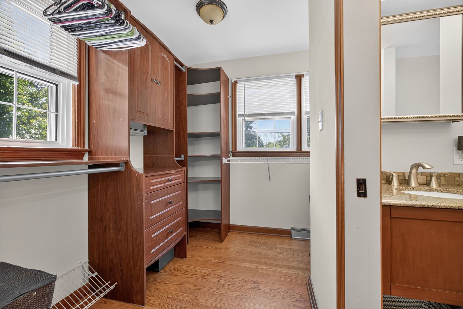 Walk-in closet with rich wood cabinetry, built-in shelving, hardwood floors, and an adjacent bathroom with sink.