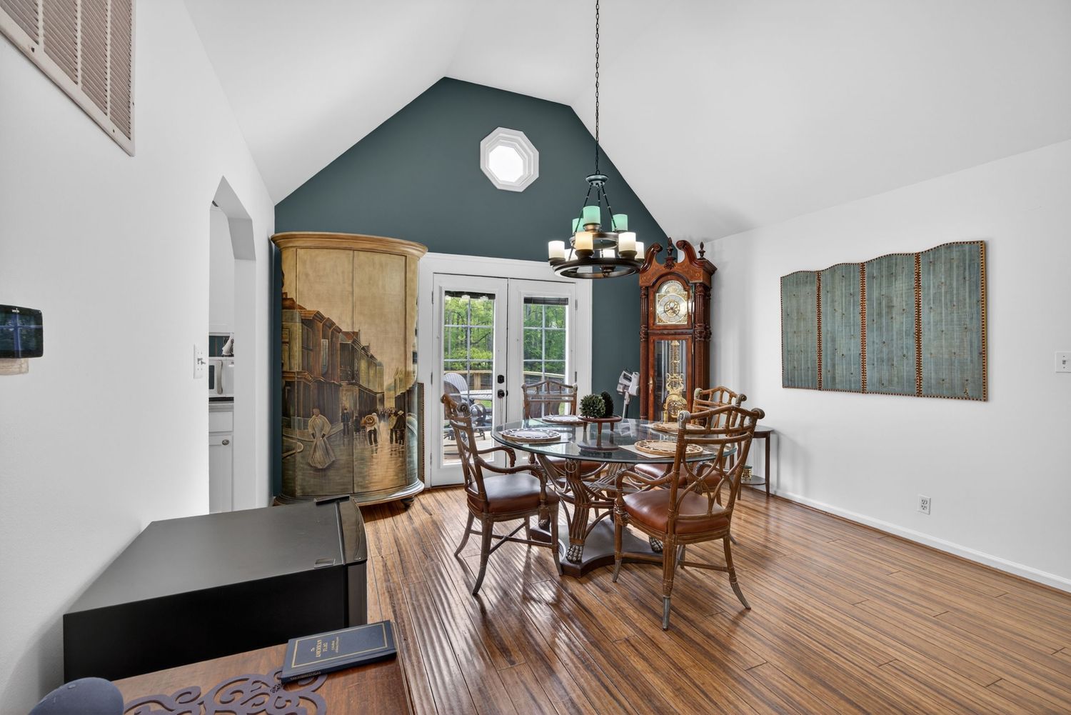Dining room with vaulted teal ceiling, hardwood floors, chandelier, wooden chairs, grandfather clock, and French doors.