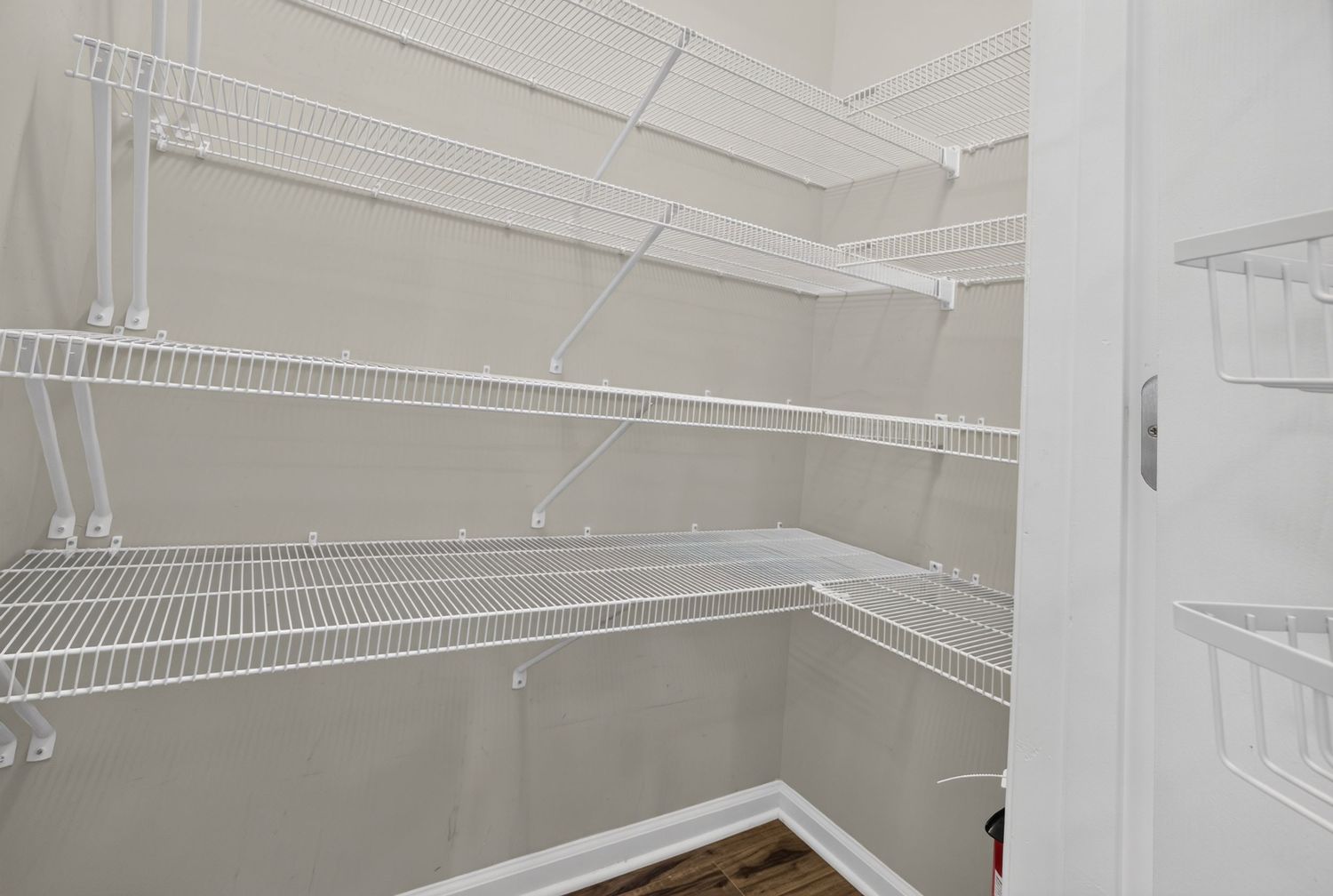 Spacious walk-in closet with white wire shelving units on three walls and hardwood flooring.