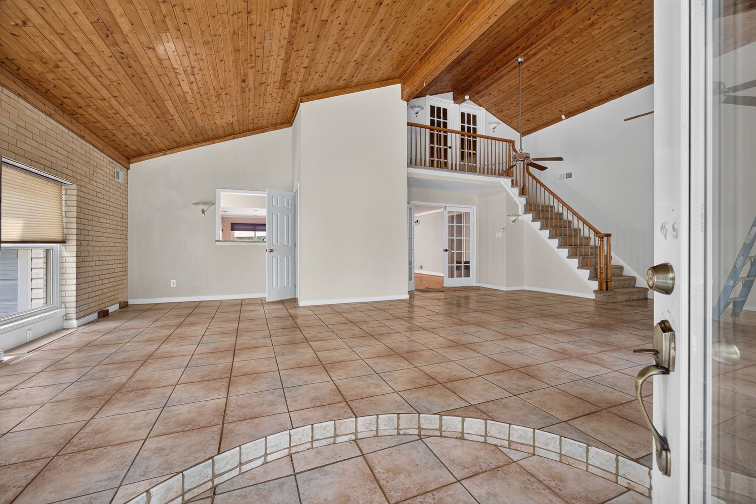 Spacious open-concept living area with beige tile floors, wood ceiling, staircase, and abundant natural light.