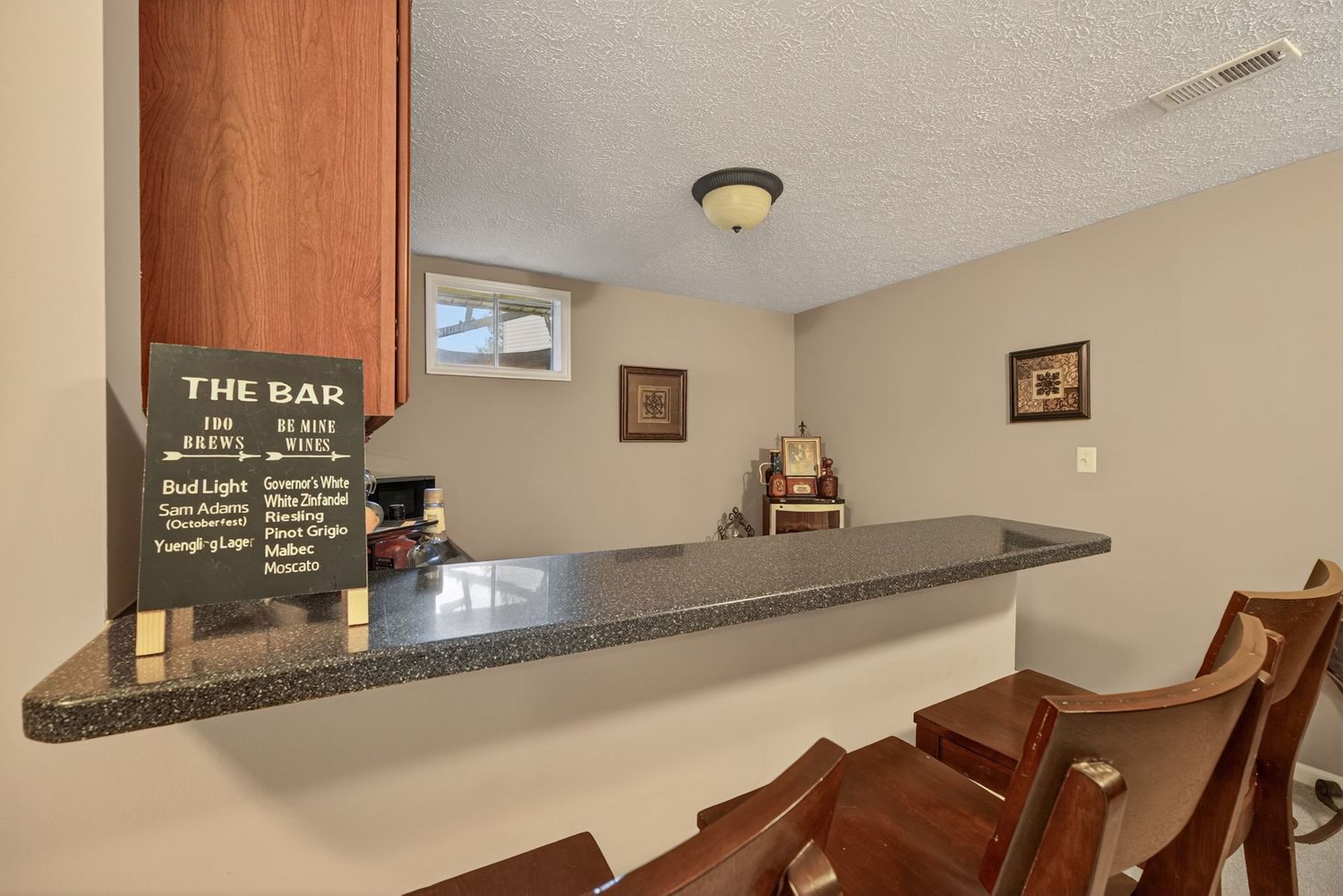Basement bar area with dark granite countertop, bar stools, and a chalkboard menu sign in a finished rec room.