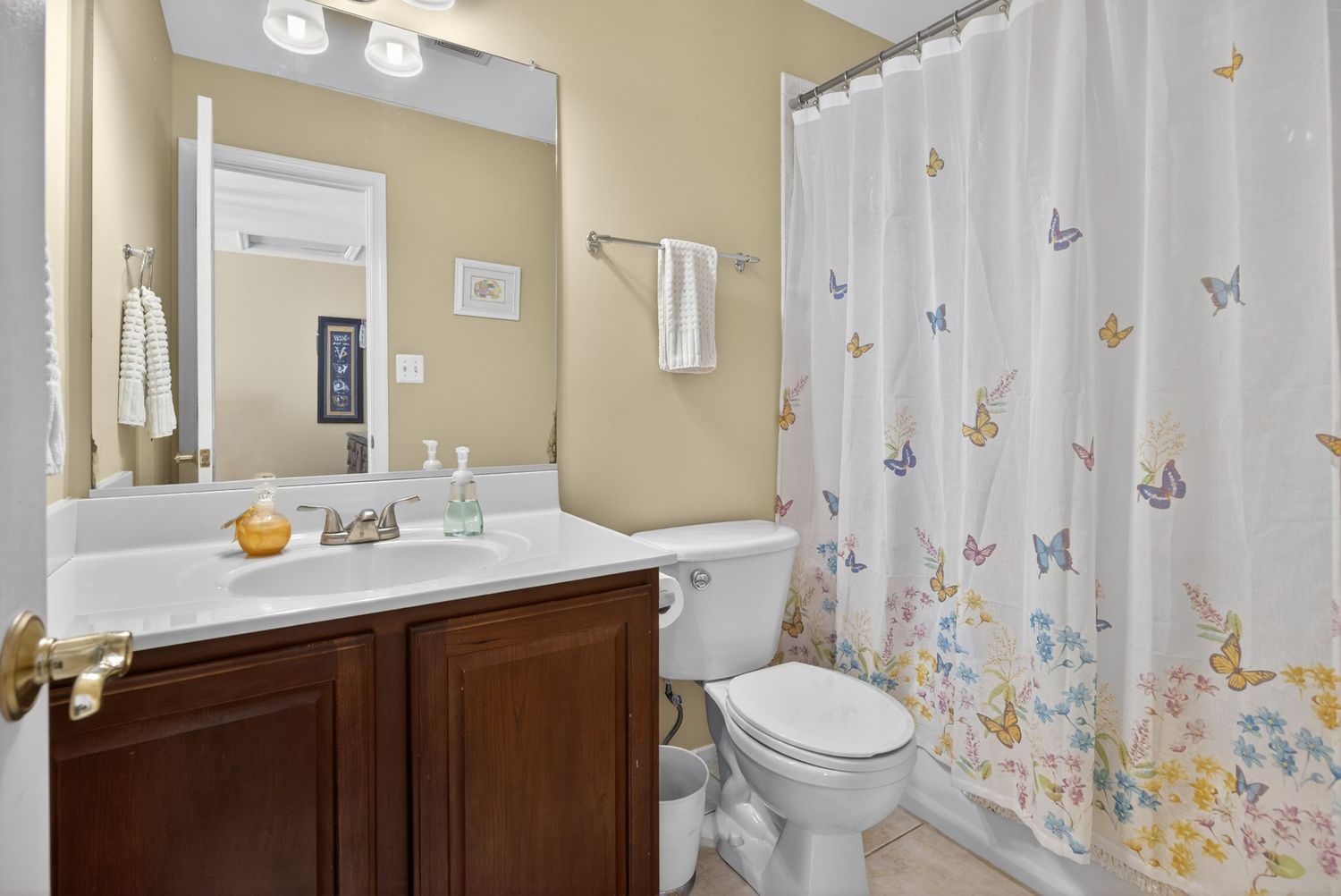Bathroom with dark wood vanity, white countertop, butterfly shower curtain, and tile flooring in a neutral-toned space.