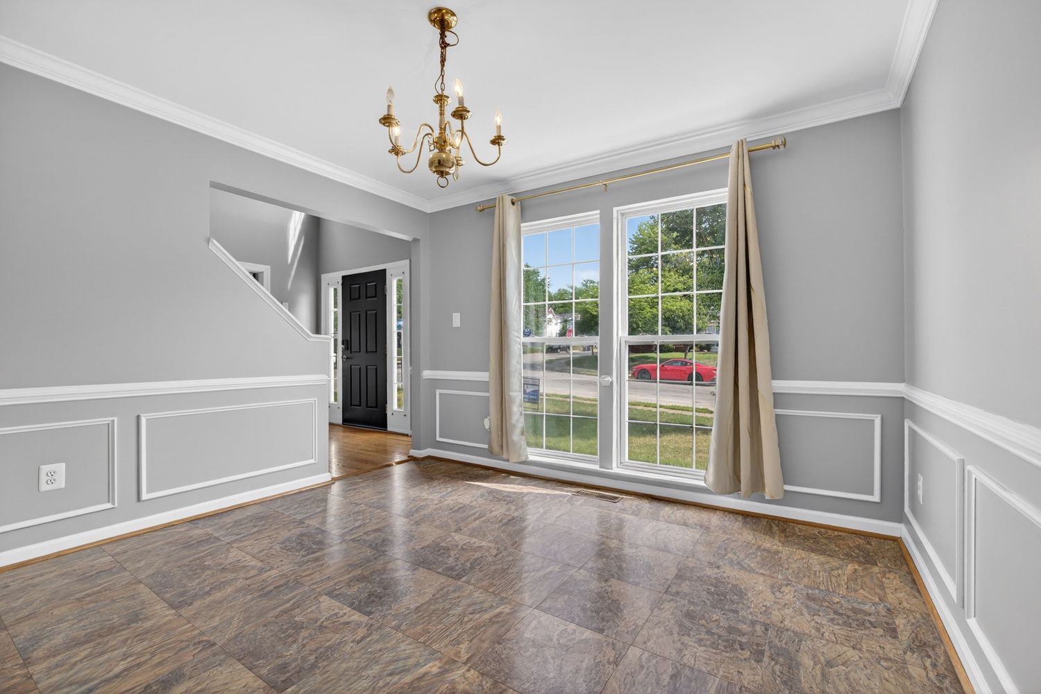 Empty dining room with wainscoting, dark tile floors, chandelier, and large window overlooking green yard.