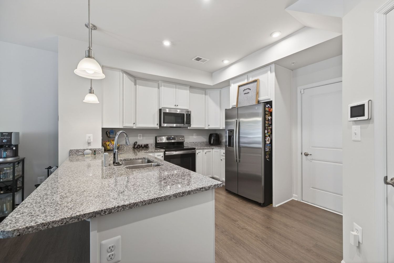 Modern kitchen with white cabinets, granite island, stainless steel appliances, and hardwood floors in a bright open layout.