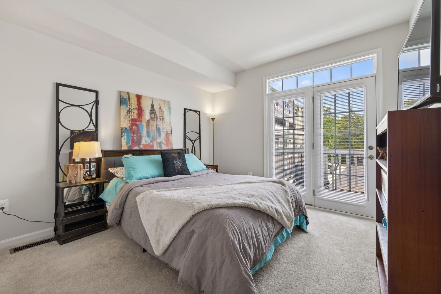 Spacious master bedroom with large windows, balcony access, gray bedding, and teal accent pillows.