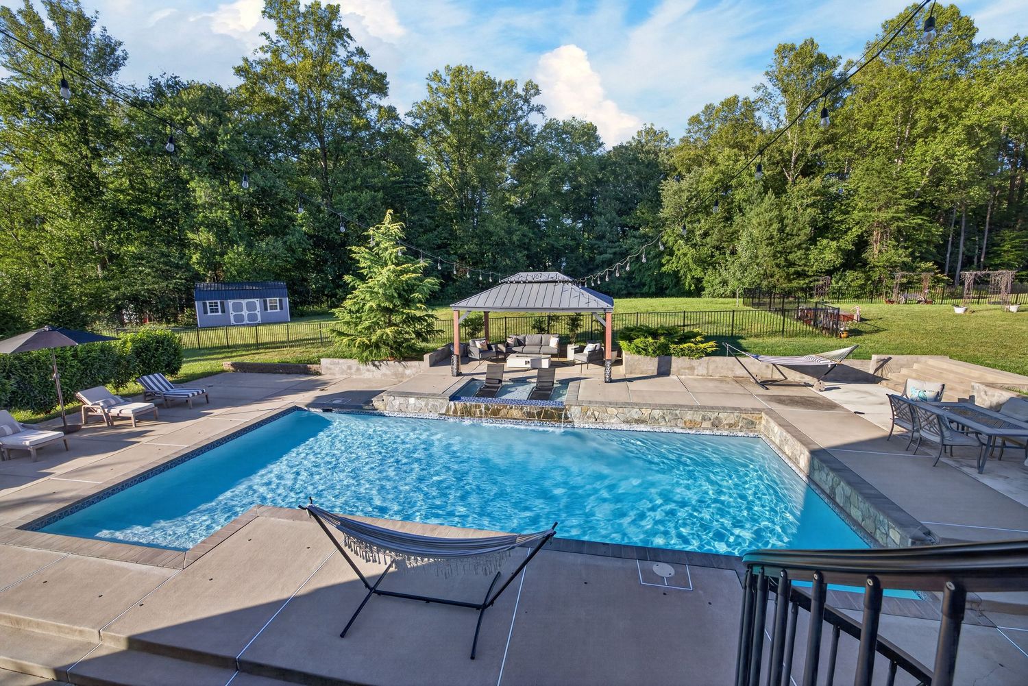 Luxury backyard pool with gazebo, lounge chairs, and lush green trees in a spacious outdoor retreat.