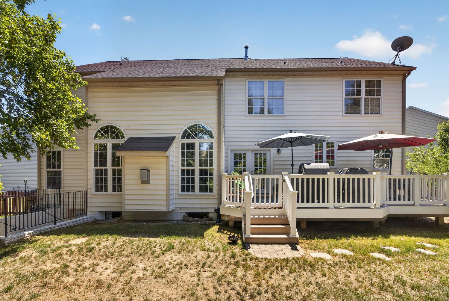 Two-story home with white vinyl siding, arched windows, and a large wooden deck with umbrella seating area.