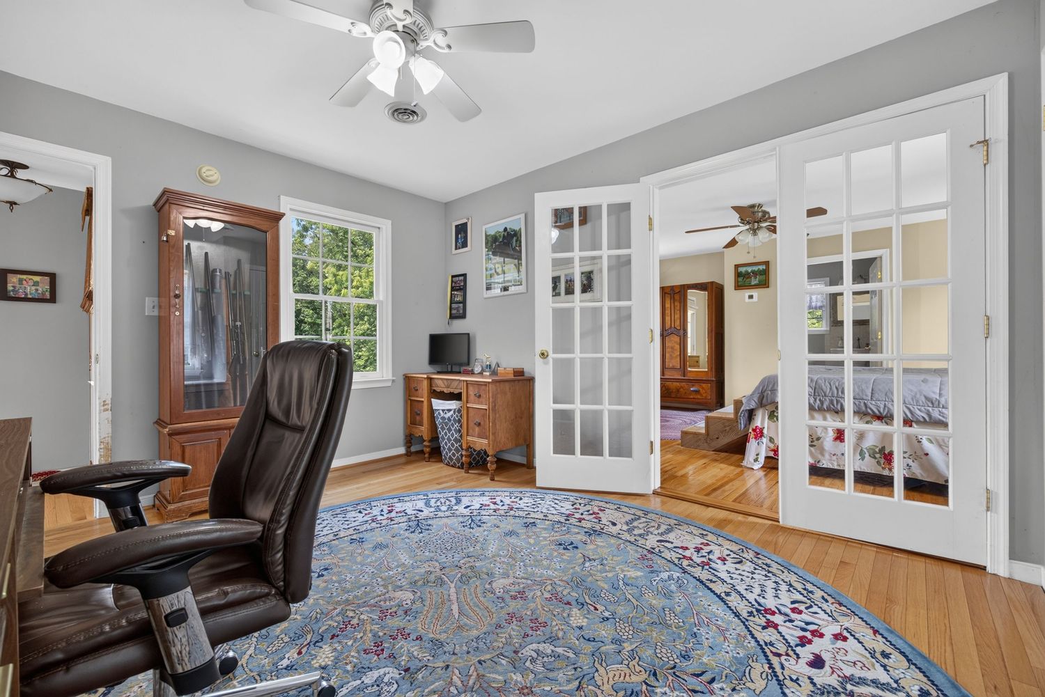 Home office with hardwood floors, round area rug, leather chair, French doors, and a window with natural light.
