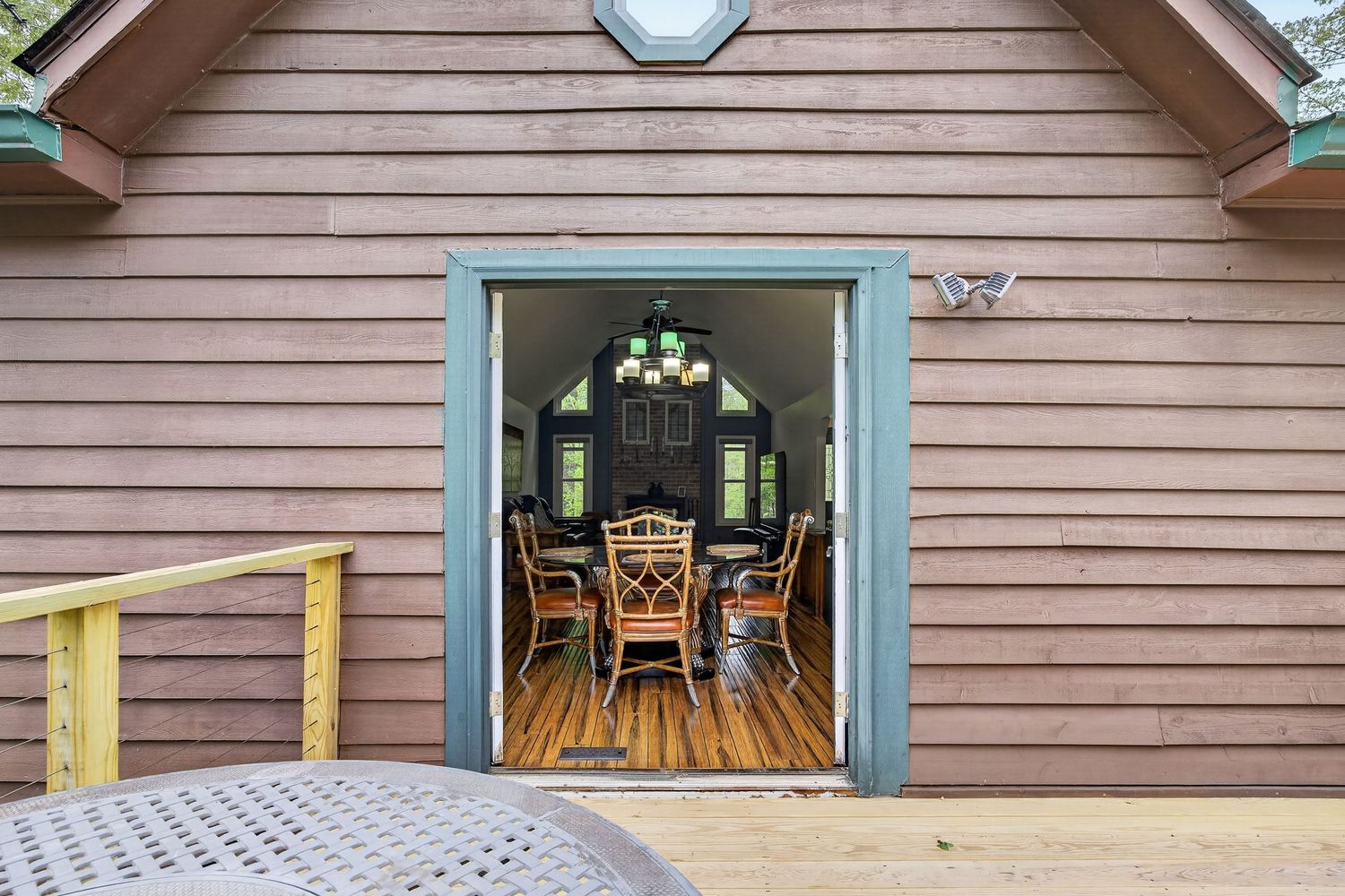 Rustic wooden cabin exterior with open sliding doors revealing a cozy dining area with wicker chairs and chandelier.