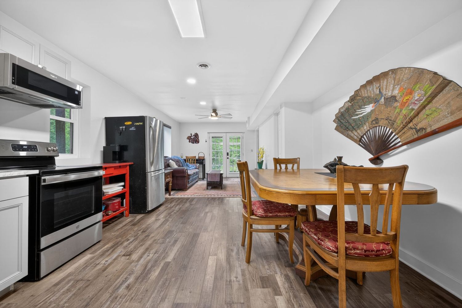 Open dining area with wood floors, round table, and view into living room and kitchen with stainless steel appliances.