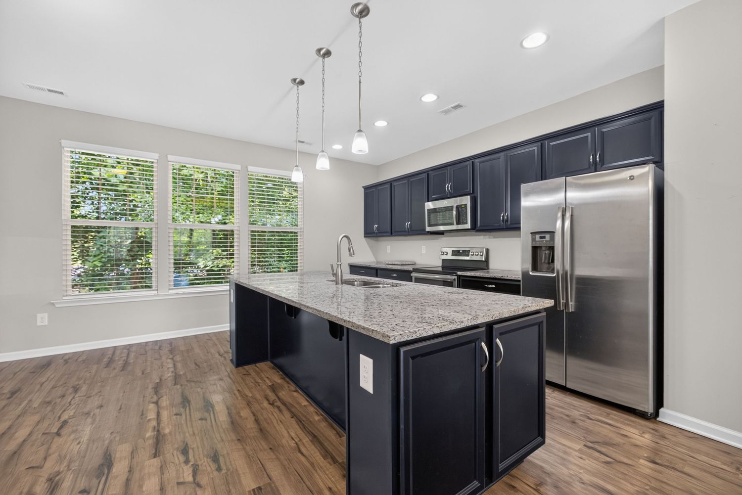 Modern kitchen with navy cabinets, granite island, stainless steel appliances, pendant lights, and hardwood floors.