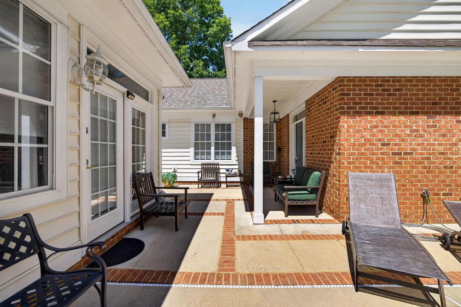 Sunny brick patio with wrought iron chairs and lounge chairs outside a white and brick home.