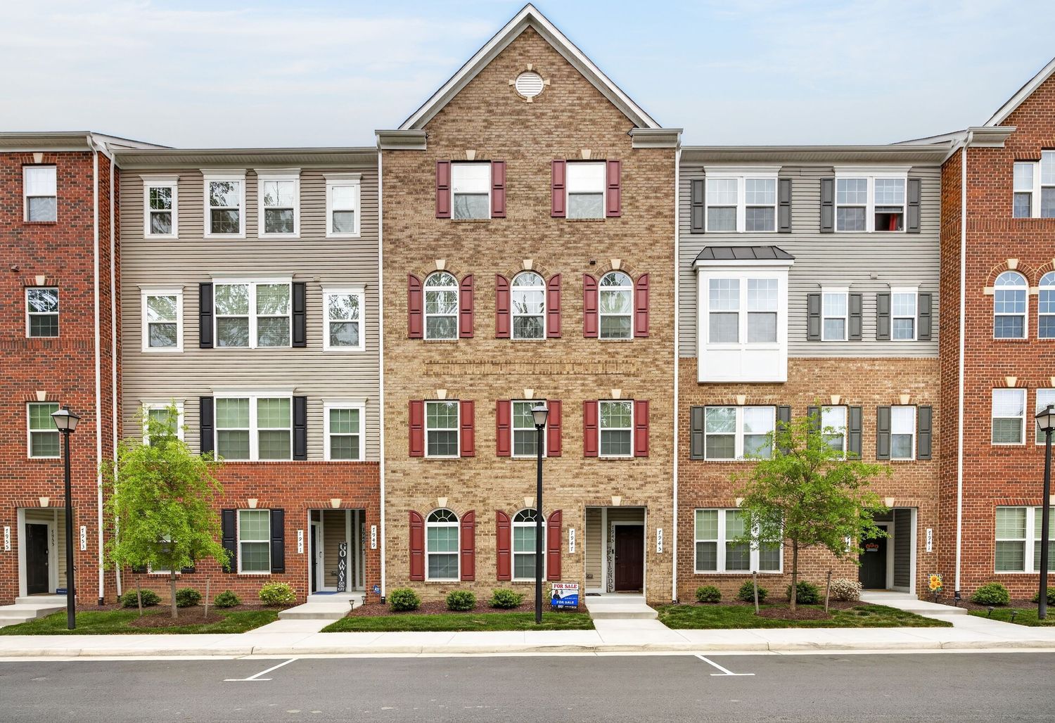 Multi-story brick townhomes with red shutters and tan siding in a modern residential community with parking lot.