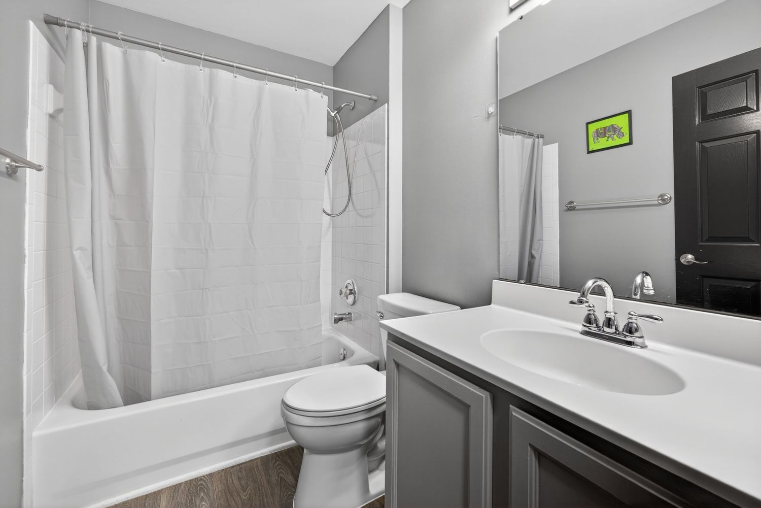 Modern bathroom with gray vanity, white quartz countertop, shower-tub combo with white curtain, and toilet.