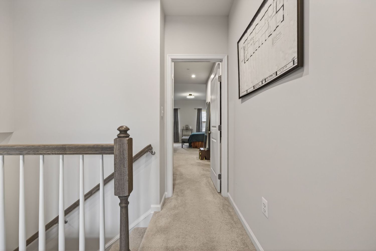 Bright hallway with carpet, white railings, and framed wall art leading to a cozy living room.